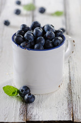 Fresh ripeblueberries in white enamel mug on white wooden rustic background
