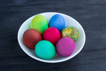 Fototapeta na wymiar White plate of Easter multicolored eggs on black wood