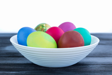 White plate with Easter multicolored eggs on black wooden background