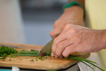 Concept: Homemade food. Closeup of human hands cutting and chopping vegetables on a domestic kitchen´s wooden table.