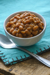 Baked beans in a white bowl with a blue napkin and spoon