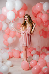 Fototapeta na wymiar Beautiful young girl in a dress among a lot of pink balls.
