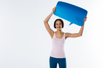 Look here. Cheerful positive young woman showing a sign and smiling while participating in the social movement