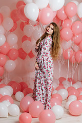 Beautiful young girl in a dress among a lot of pink balls.