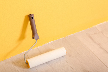 Paint roller for interior decorating on floor near color wall
