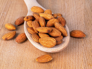 heap of almond in wooden spoon on wooden background, side view