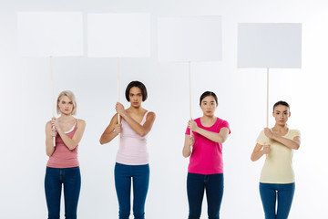 Fototapeta premium Serious issue. Smart pleasant attractive women looking at you and holding signs while being serious about social issues