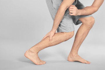 Young man suffering from pain in leg on grey background