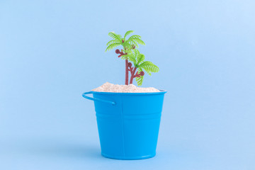 Can with sand and plastic palm tree isolated on blue background. Summertime vacation minimalistic still life concept.
