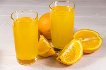 Glass of orange juice and fresh oranges on white wooden table