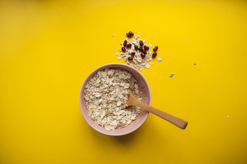 Oatmeal with wooden spoon and pomegranate seeds on bright yellow background.