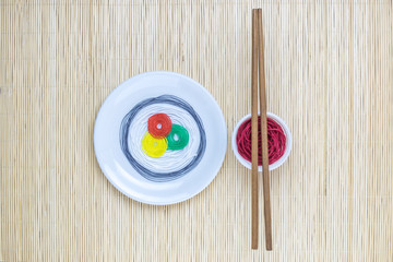 Strings in different colors in form of sushi roll and soy sauce with sticks on beige bamboo mat minimalistic abstract concept