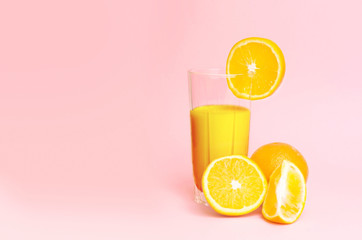 A glass with orange juice with the cut oranges on a pink background. Juicy color scale, pin up, pop up styles. Food for breakfast, a healthy drink with vitamins and miniroalami. A sunny drink.