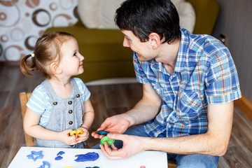 Picture of a father and daughter playing with color play dough and cutters. Having fun with colorful modeling clay. Creative kids molding at home. Children play with plasticine or dough.