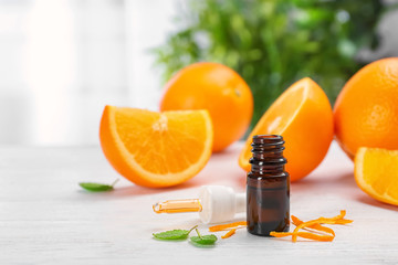 Bottle with essential oil and fresh oranges on table against blurred background