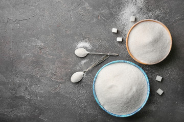 Bowls and spoons with pure sugar on grey background