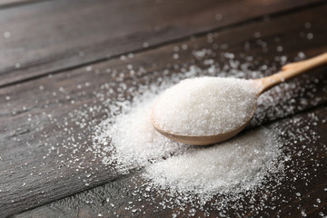 Spoon with pure sugar on wooden background