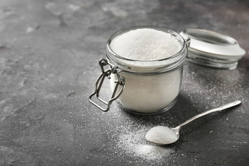 Glass jar with pure sugar on grey background