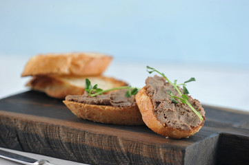  In the frame there is a wooden board and baguette slices. Slices of baguette with liver pate.