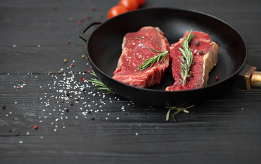 Raw fresh ribeye steak with salt, seasonings, and rosemary in a frying pan wooden background