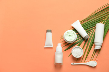 Different skin care cosmetic products with green leaf on color background, top view