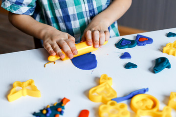 Close up picture of a child playing with  color play dough and cutters. Having fun with colorful modeling clay. Creative kids molding at home. Child's hands rolling up plastiline