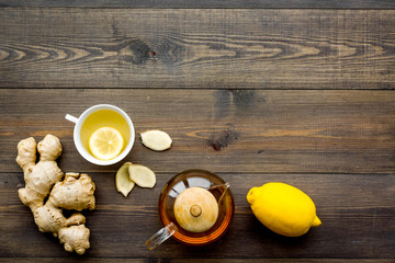 Tea for cure colds. Cup, teapot, ginger root and lemon on dark wooden background top view copy space