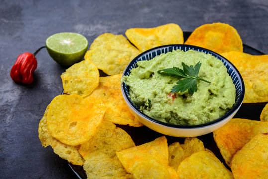 Guacamole with chips and fresh lime and pepper on dark background