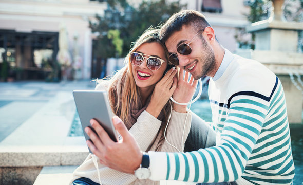 Happy couple listening to music with tablet and headphones outdoors. Dating, love and tenderness, lifestyle concept