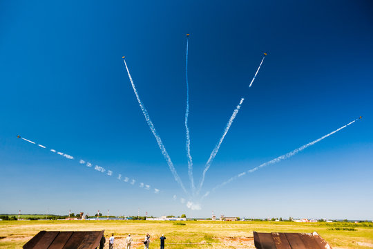 A group of professional pilots of military aircraft of fighters on a sunny clear day shows tricks in the blue sky, leaving beautiful traces of clouds scattered in different directions.