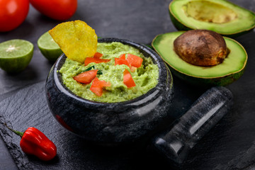 Guacamole with chips and fresh ingredients on dark background