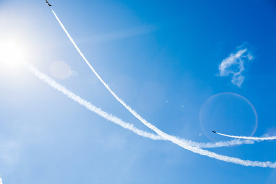 A group of professional pilots of military aircraft of fighters on a sunny clear day shows tricks in the blue sky, leaving beautiful traces of clouds scattered in different directions.