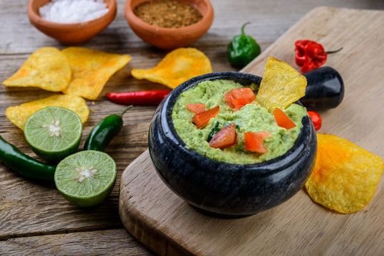 Guacamole with chips and fresh ingredients on a rustic wooden background