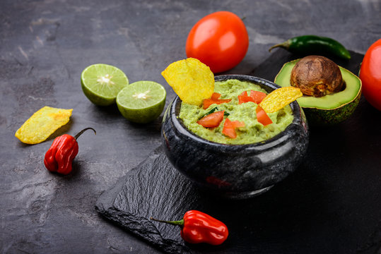 Guacamole with chips and fresh ingredients on dark background