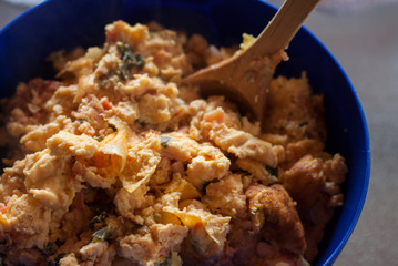 Concept: Homemade food. Scrambled eggs with tomato, onion and herbs homemade ready to be served in a plastic blue bowl. Food background texture.