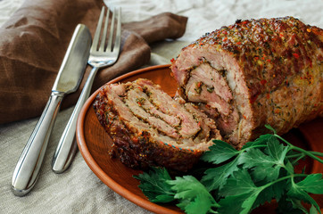 on a clay plate lies a cut meatloaf with a juicy middle, beside a brown linen napkin, a crumpled light linen tablecloth, a fork, a spoon