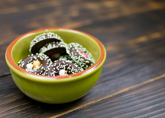 Multicolored cookies in a plate on a dark wooden background.