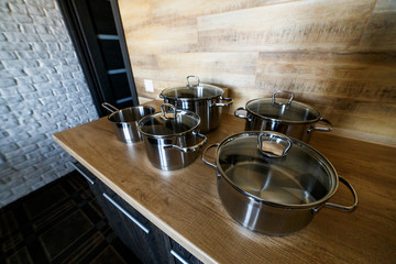 Image of kitchen ware. Set of shiny stainless steel saucepans big and small on wooden surface