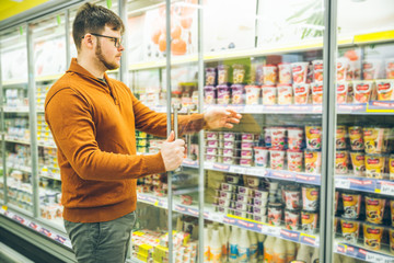man takes yogurt from fridge. grocery shopping concept