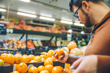 man choose oranges from shelf of store.