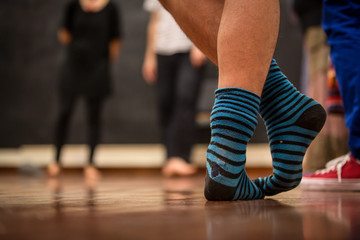 Experienced teacher explaining a dance position. Feet standing closeup with blue and black striped socks in a room full of people. Concept: Teaching how to do it.