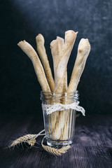 Italian breadsticks lit by moonlight are on a wooden table in a glass cup 