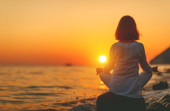woman practices yoga and meditates in lotus position on sunset beach.