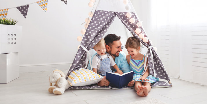 family father reading to children book in tent at home.
