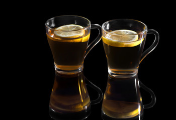 Black tea with a lemon in a glass cup, with reflection on a black background.