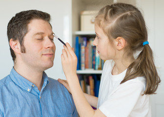 Cute little girl making makeup to her dad.