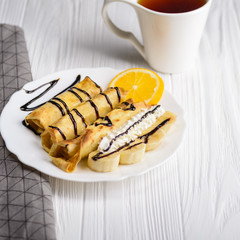 Pancakes with banana, whipped cream decorated with chocolate syrup on white wooden background. And a cup of tea