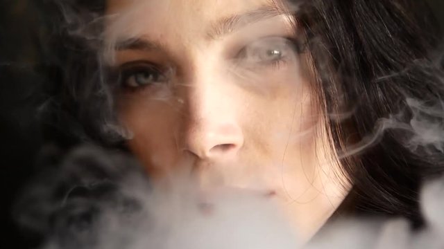 Close up of woman mouth smoking. The girl slowly and sexually releases smoke from an electronic cigarette
