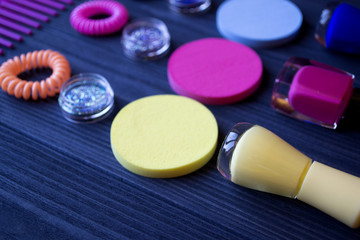 Obraz na płótnie Canvas Colorful and bright cosmetics. Beauty care tools. Beauty salon. Girl's paradise. Nail polishes, sequins, pink hair bands and comb on a dark blue wooden desk. Bright still life of beauty instruments.