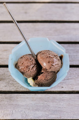 Sundae with scoops of vanilla and chocolate ice cream served in blue plastic cup with stainless steel spoon on wooden garden table